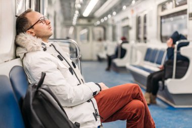 Beyaz ceketli ve bordo pantolonlu yakışıklı adam eve giderken metro vagonunda uyuyakalmış. Adamın yanında siyah bir sırt çantası var. Yoğun çalışma günü, stres, yorgunluk, aşırı çalışma..