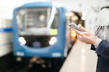 Adam akıllı telefonu elinde tutuyor, sohbet ediyor, mesajlar yolluyor, tren beklerken internette sörf yapıyor. Yaklaş, seçici odaklanma. İnsanlar, iletişim ve teknoloji kavramı.