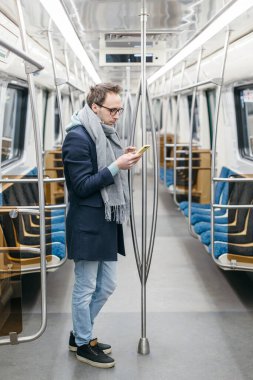 Gözlüklü yakışıklı metro treninde tek başına geziyor. Mavi bir ceket, gri bir eşarp ve siyah bir spor ayakkabı giyiyor. Elinde cep telefonu tutuyordu. Dijital bağımlılık, sosyal ağlar bağımlılığı.