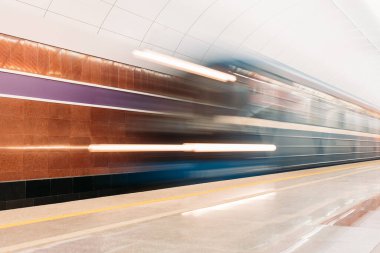 Bulanık mavi trenin metro istasyonuna girişinin fotoğrafı. Metro platformu farklı renklerde mermerle dekore edilmiş. Kentsel konseptte toplu taşıma ve hareketlilik.