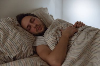 Giyinik yetişkin erkek portresi, yorgunluk / sosyal medya bağımlılığı, yorgun adam, birikmiş yorgunluk, uykusuzluk, sağlık sigortası konsepti nedeniyle elinde telefonla yatakta uykuya daldı..