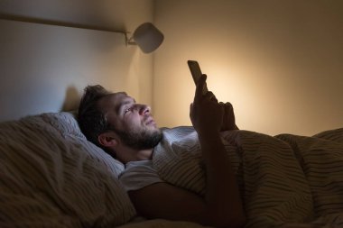 Yetişkin uykulu bir adamın portresi sırtüstü yatar ve ağ / internet tuzağında sörf yapar sosyal medya bağımlılığı, yarı kapalı gözler, uyku bozukluğu, cep telefonuna bağımlılık, uykusuzluk konsepti.