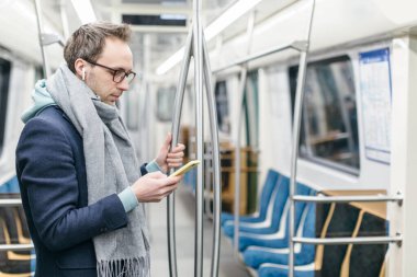 Gözlüklü ve kablosuz kulaklıklı genç adam metro trenine biniyor. O, mavi bir ceket ve gri bir eşarp giyiyor. Elinde cep telefonu tutuyordu. Dijital bağımlılık, sosyal ağlar bağımlılığı.