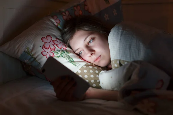 Genç uykulu yorgun kız gece geç saatlerde akıllı telefon kullanarak yatakta uzanıyor, uyuyamıyor. Sosyal medya bağımlılığı, cep telefonu bağımlılığı, uykusuzluk, nomofobi, uyku bozukluğu, uykusuzluk konsepti.