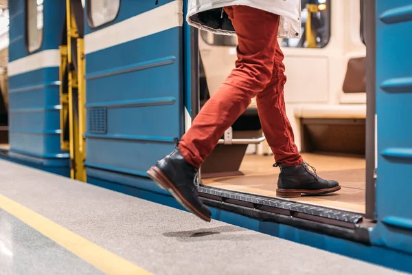 Handsome man in black shoes, burgundy pants and white jacket runs into a subway train. Male is late for work. Selective focus on the left leg. Public transport and mobility in urban concept. Close up.