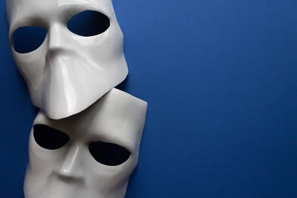 Divadelní koncept s bílými maskami na klasickém modrém pozadí. Anonimní, inkognito, konspirační koncept. Místo pro text. Plochý styl. Horní pohled — Stock fotografie