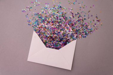 Pastel leylak arka planında çok renkli, parıltılı konfeti harfleri olan beyaz bir zarf. Kutlama konsepti. Düz yatış stili. Üst görünüm