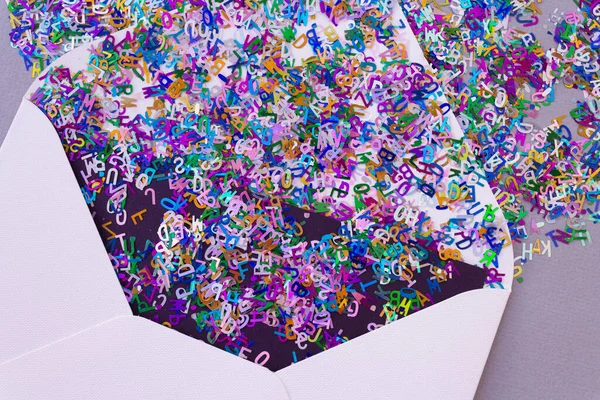 Enveloppe blanche ouverte avec des lettres de confettis scintillantes multicolores sur fond lilas pastel. Concept de salutation festive. Style à plat. Vue du dessus — Photo