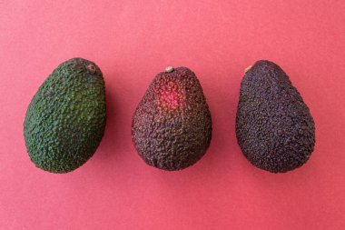 Kırmızı arka planda farklı olgunlukta avokado. Düz yatış stili. Kapatın. Metin için yer