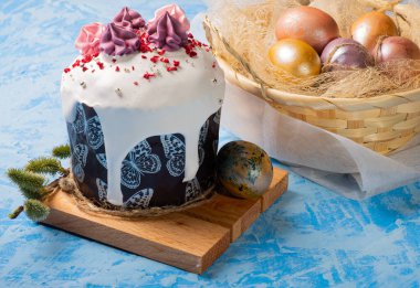 Geleneksel Paskalya pastası yakın plan, arka planda beyaz kremalı pişirme Paskalya yumurtaları, mavi doku arka plan.