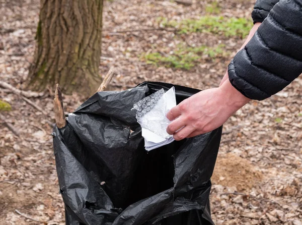 Hand throwing crumpled paper in the litter bin in the forest, garbage collection in the forest