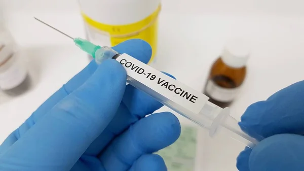 Mavi koruyucu eldivenli bir el, araştırılmış bir koronavirüs aşısını tutuyor.