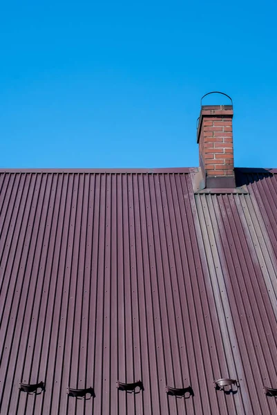 Металлическая крыша с кирпичным дымоходом - голубое небо в качестве фона — стоковое фото