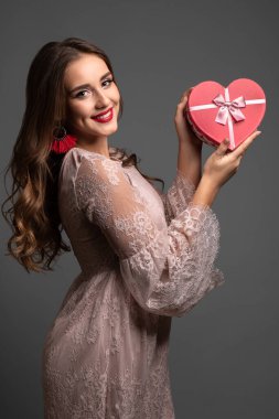 Soluk pembe elbiseli, uzun kıvırcık saçlı genç ve güzel bir kız. Elinde hediyeyle kameraya bakıyor. Stüdyo çekimi. 