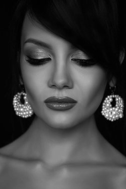 Göz kapaklarını özenle indiren profesyonel makyajlı ve inci küpeli güzel bir esmerin yakın portresi. Siyah beyaz fotoğraf..