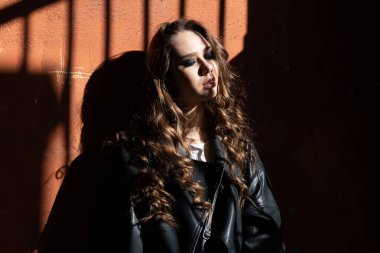 Açık hava portresi, şehir gölgeleriyle aydınlık bir genç kadın inanılmaz makyajlı, modaya uygun siyah ceket giyiyor. Kapatın. Metin uzayı.