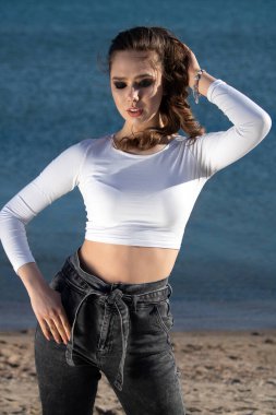 Deniz kıyısında yürüyen ve günbatımında güneşlenen inanılmaz makyajlı genç bir kadının açık hava portresi..