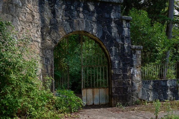 Stone fence with iron gates in the trees. — Stock Photo, Image