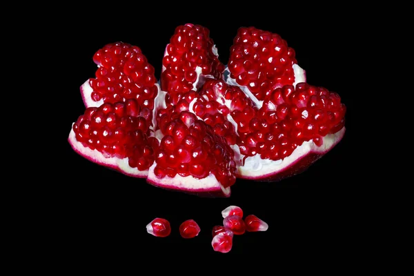Open ripe pomegranate fruit with bright red grains close up isolated on a black background