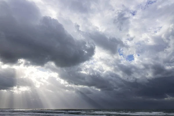 Sunbeams breaking through the clouds of a dramatic stormy sky over the Mediterranean Sea with foamy waves — Stock Photo, Image