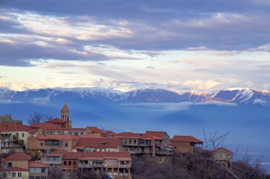 Sighnaghi şehri karla kaplı dağların ve bulutların ardında duran bir tepenin üzerinde duruyor.