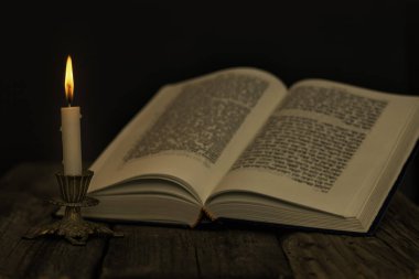 Tevrat 'ı aç ve bir şamdanda yanan bir mum. Karanlık bir arka planda, ahşap bir yüzey üzerinde.