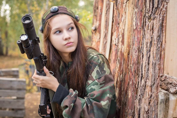 Young girl with a gun peeking from behind cover — Stock Photo, Image