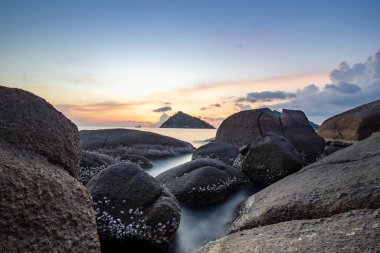 Deniz kenarında, kumlu kayaların arasında gün batımı