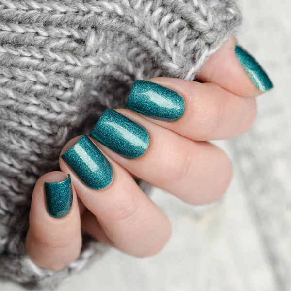Bright turquoise manicure with holography on the background of a gray knitted sweater — Stock Photo, Image