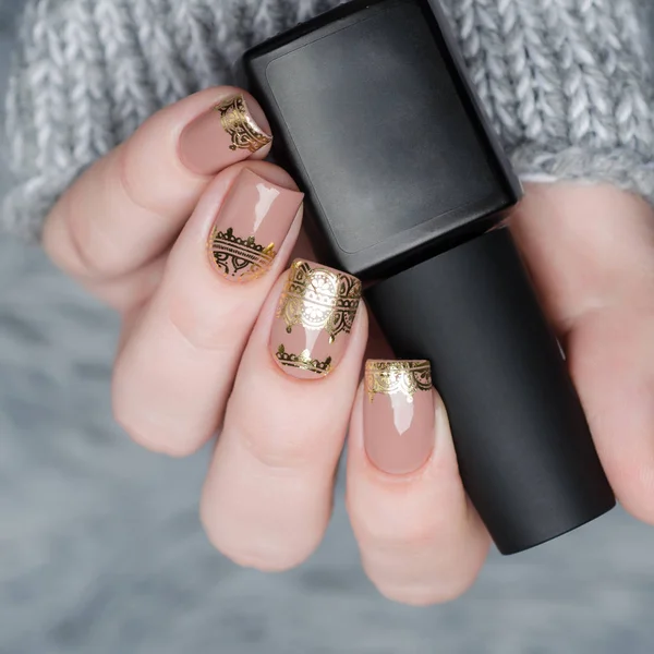 Beige Nude manicure with gold lace pattern on a gray background — Stock Photo, Image