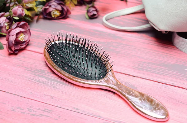 Pink hairbrush on a pink wooden background with flowers — ストック写真