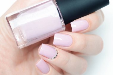 Hassas pastel pembe manikür ve beyaz arka planda yapay elmaslar.