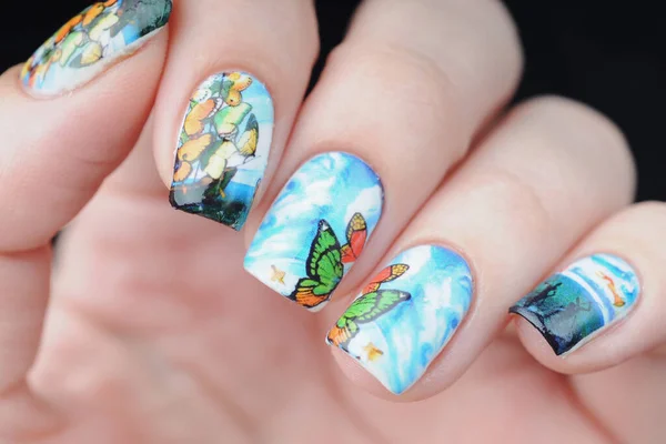 Manicure azul da cor com impressão da borboleta com nuvens, mar do oceano e navio Imagem De Stock