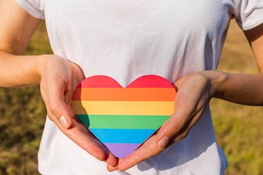 Kadın elinde gökkuşağının renginde bir kalp tutuyor. Genç, güzel bir kız. Lgbt tarihi ayı. Gurur Ayı. Lezbiyen Gey Biseksüel Transseksüel. Lgbt bayrağı. Aşk, insan hakları, hoşgörü. Lgbtq+