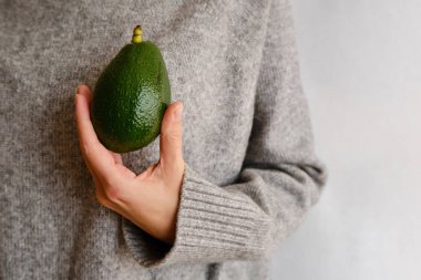 Bir kadın elinde yeşil avokado tutuyor. Avokado yakın çekim. Doğal taze organik egzotik meyve. Sağlıklı beslenme, çiğ gıda diyeti. Vejetaryen yaşam tarzı. Düzgün beslenme. Yemek hazır. Eko ürün. Poster