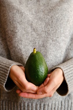 Bir kadın elinde yeşil avokado tutuyor. Avokado yakın çekim. Doğal taze organik egzotik meyve. Sağlıklı beslenme, çiğ gıda diyeti. Vejetaryen yaşam tarzı. Düzgün beslenme. Yemek hazır. Eko ürün. Poster