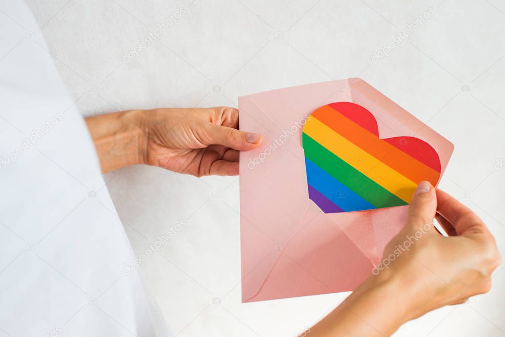 Woman holds in hands envelope and heart in the colors of the rainbow. Young beautiful girl. LGBT pride month. Coming out. Lesbian Gay Bisexual Transgender. LGBTQ+ flag. Love, human rights, tolerance
