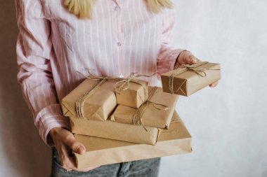 Elinde bir sürü hediye kutusu tutan bir kadın. Tatil hediyesi. Sürpriz dolu kutular. Kutlamanız kutlu olsun. Kraft kağıt ambalajı. Paket kağıdı ve kurdele. Kutulara yakın duran kadın eli. Tebrikler.