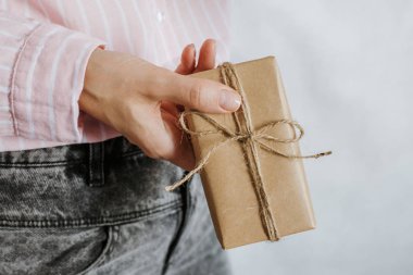 Kadın hediyeyi elinde tutuyor. Tatil hediyesi. Sürpriz boks. Kutlamanız kutlu olsun. Kraft kağıt ambalajı. Paket kağıdı ve kurdele. Kadın eli, yakın çekimde. El yapımı tebrik.