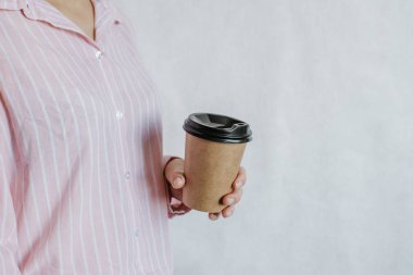 Elinde kahve ya da çayla kağıt bardak tutan bir kadın. Kahve zamanı. Tek kullanımlık kağıt bardak. Güzel sarı saçlı genç kız. Sıradan tarz, beyaz gömlek ve kot pantolon. Götürün. Sıcak içecek. Boşluk alanı