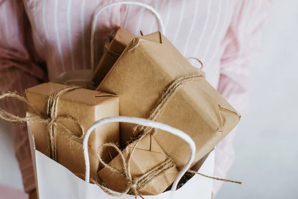 Woman holding many gift boxes in hand. Holiday present. Boxes with surprise. Happy celebration event. Kraft paper packaging. Wrapping paper and ribbon. Female hand with boxes close-up. Congratulation