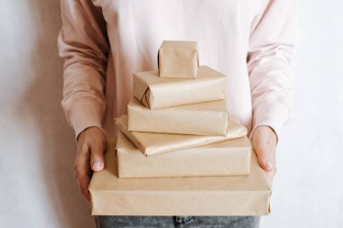 Elinde bir sürü hediye kutusu tutan bir kadın. Tatil hediyesi. Sürpriz dolu kutular. Kutlamanız kutlu olsun. Kraft kağıt ambalajı. Paket kağıdı ve kurdele. Kutulara yakın duran kadın eli. Tebrikler.