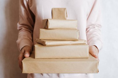 Elinde bir sürü hediye kutusu tutan bir kadın. Tatil hediyesi. Sürpriz dolu kutular. Kutlamanız kutlu olsun. Kraft kağıt ambalajı. Paket kağıdı ve kurdele. Kutulara yakın duran kadın eli. Tebrikler.