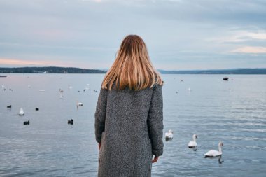 Güzel sarı saçlı kadın Bodensee Gölü kıyısında manzaranın tadını çıkarıyor. İsviçre 'de manzara. Seyahatte mutlu bir kız. İnanılmaz manzaralı açık hava manzarası. Dramatik bir gökyüzü. Sudaki kuğular. Macera yaşam tarzı, özgürlük