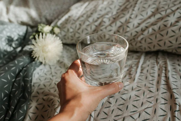 Woman in bed holding a glass of water in hand. Happy morning. Girl in pajamas. Healthy lifestyle, wellness. Proper nutrition. Drinking water. Morning with water. Sunlight on linens. Pillow, blanket