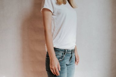 Blond hair woman posing near a light wall. Beautiful young caucasian girl. Hand gestures. Emotion. Casual clothing. Studio model in work. Strong woman, future is female. Jeans and white blank t-shirt