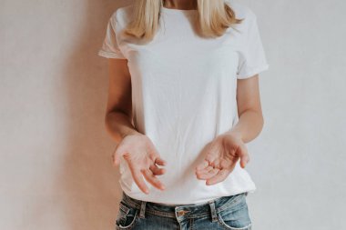 Blond hair woman posing near a light wall. Beautiful young caucasian girl. Hand gestures. Emotion. Casual clothing. Studio model in work. Strong woman, future is female. Jeans and white blank t-shirt