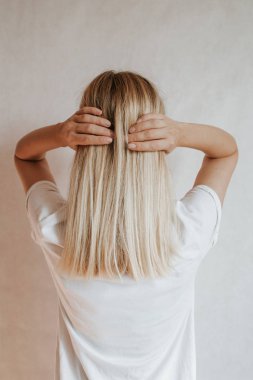 Blond hair woman posing near a light wall. Beautiful young caucasian girl. Hand gestures. Emotion. Casual clothing. Studio model in work. Strong woman, future is female. Jeans and white blank t-shirt