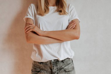 Blond hair woman posing near a light wall. Beautiful young caucasian girl. Hand gestures. Emotion. Casual clothing. Studio model in work. Strong woman, future is female. Jeans and white blank t-shirt