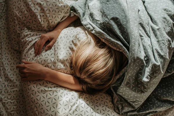 Woman sleep in bed. Blond hair girl under blanket on pillow. Wake up. Dreaming. Happy morning in bedroom. Cozy and comfortable. Sunlight on bed linen. Pillow, blanket. Recovery, relax, lifestyle
